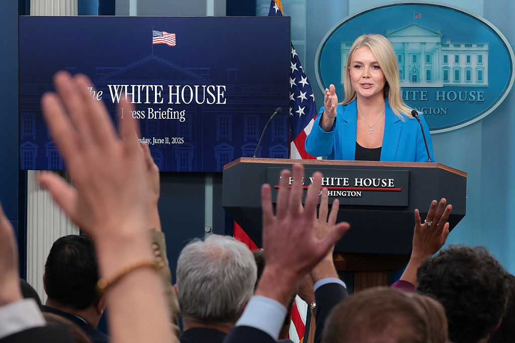 A woman speaks at a White House press briefing podium as audience members raise their hands