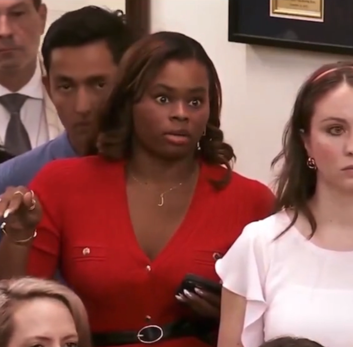 Person in a red dress looks surprised in a crowded indoor setting, holding a phone