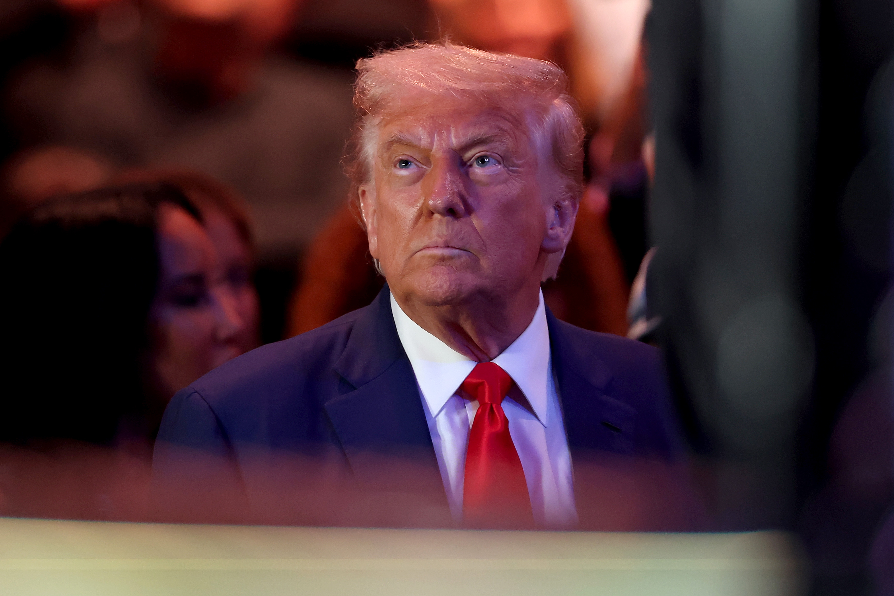 Donald Trump in a suit with a tie looks upward with a serious expression at a public event