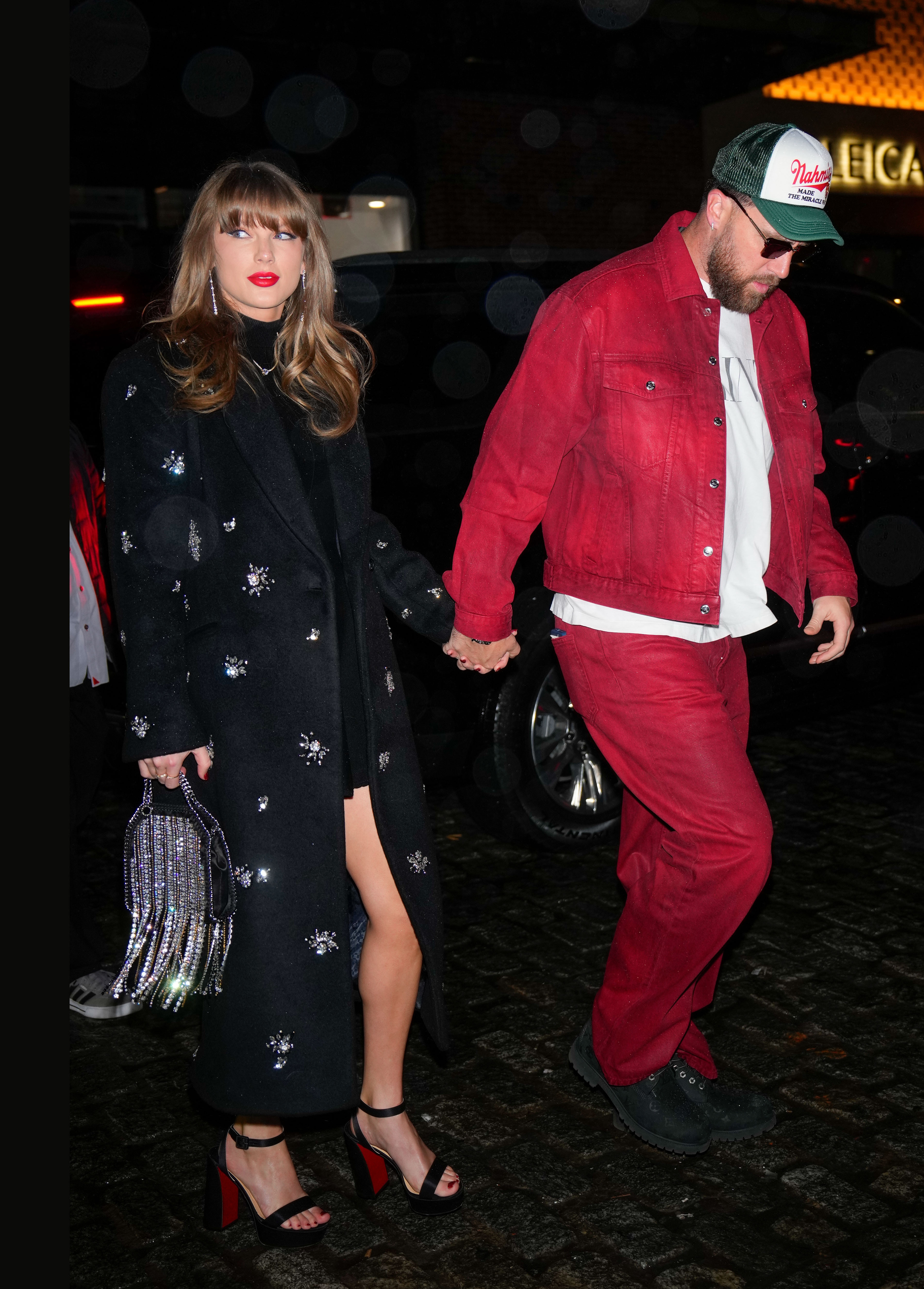 Taylor Swift in a long sparkly coat and matching fringe bag holding hands with Travis Kelce