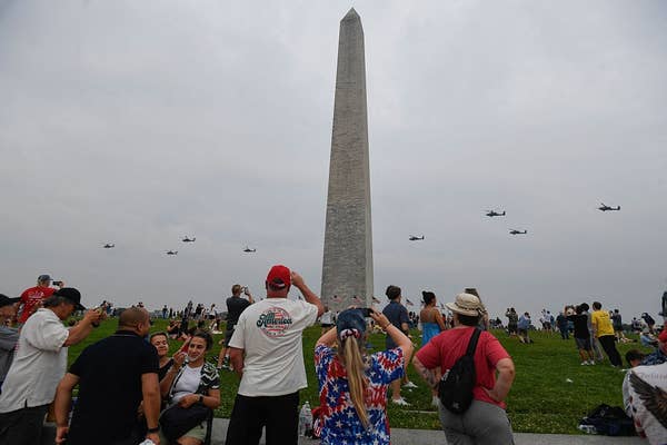 People watching helicopters flying near the Washington Monument during an outdoor event