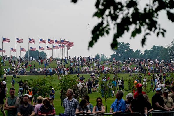 Crowd gathered on a grassy hill with numerous American flags flying in the background, suggesting a public event or celebration