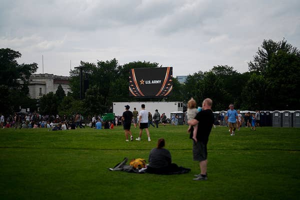 People relax on a lawn at an outdoor event, with a large screen showing &quot;U.S. Army&quot; in the background
