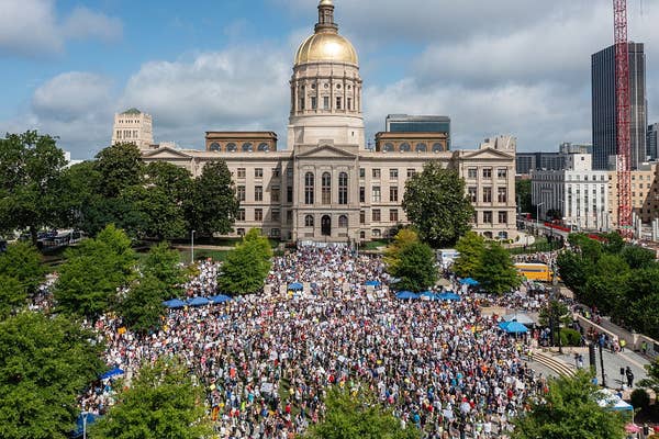 Large crowd gathered peacefully in front of a historic government building, participating in a public demonstration event