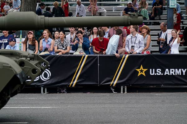 A large crowd sits behind a barrier marked &quot;U.S. Army,&quot; watching a tank on a street during a public event