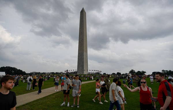 People gather near the Washington Monument on a cloudy day, engaging in outdoor activities and sightseeing
