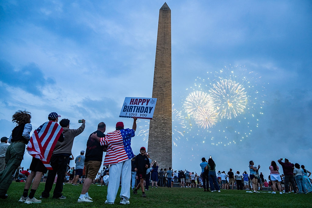 People watch fireworks near the Washington Monument, celebrating a birthday with a sign that says "Happy Birthday. I Love You."