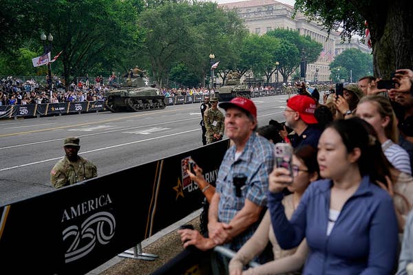 People watching a parade featuring military tanks on a street lined with spectators and officials