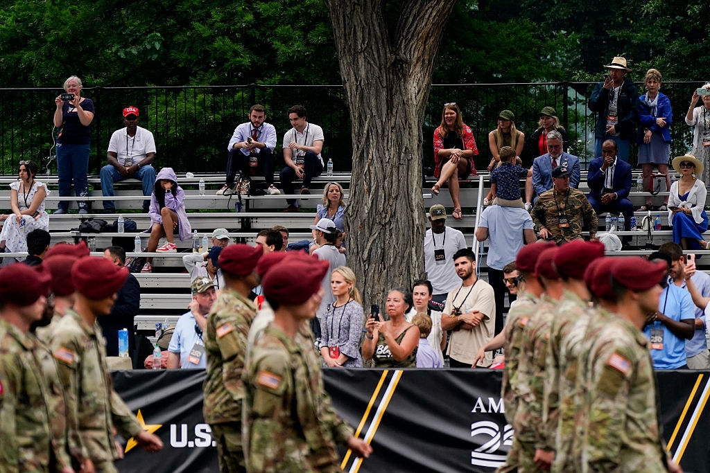 Soldiers in berets march in front of spectators seated on bleachers during an outdoor event