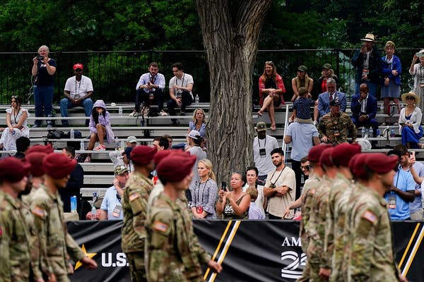 Soldiers in berets march in front of spectators seated on bleachers during an outdoor event