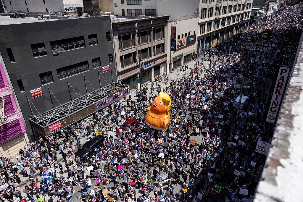 Aerial view of a large protest with a giant inflatable duck in the crowd, filling a city street with people holding signs
