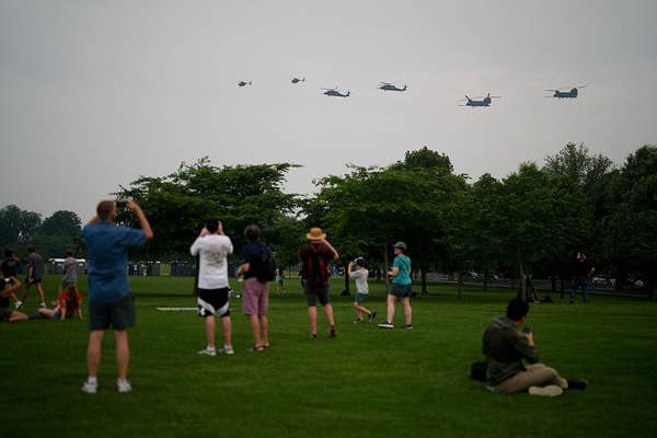 People watch helicopters flying in formation over a park, capturing photos and videos