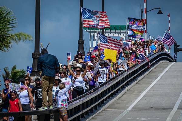People marching across a bridge holding signs and American flags, participating in a demonstration