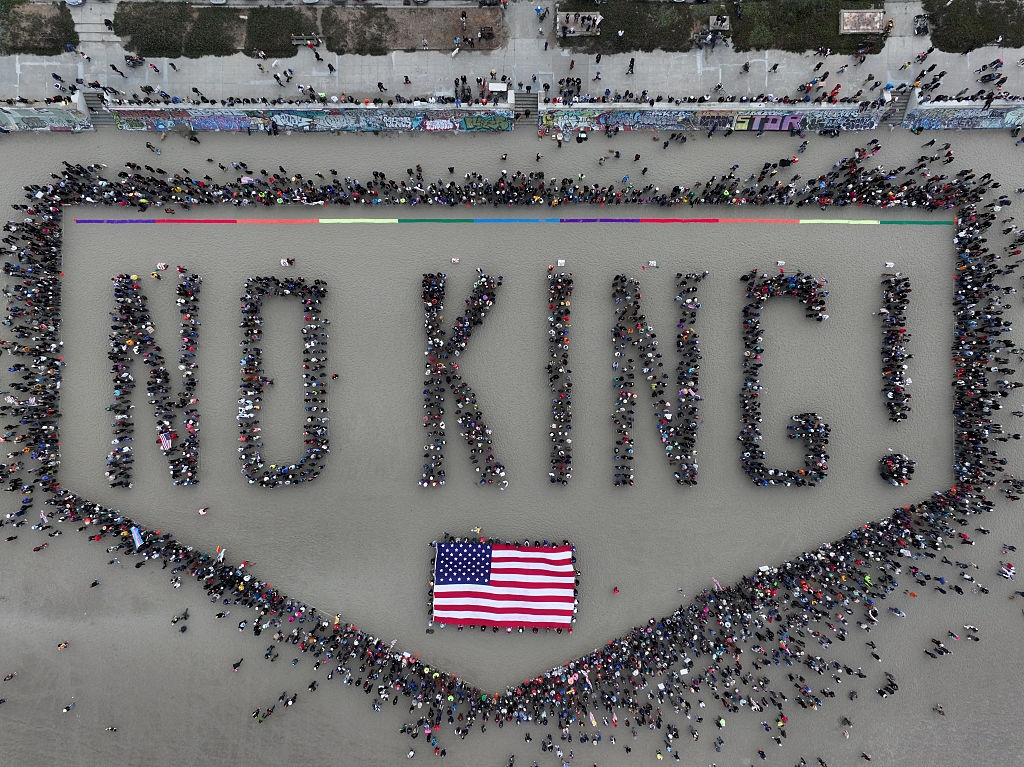 Aerial view of a large crowd forming the words "NO KING!" around a U.S. flag on the ground in a public space