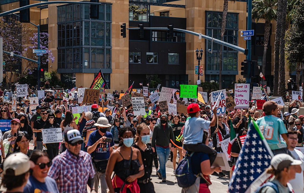 A diverse crowd of protesters holding signs marches in a city street, advocating for various causes