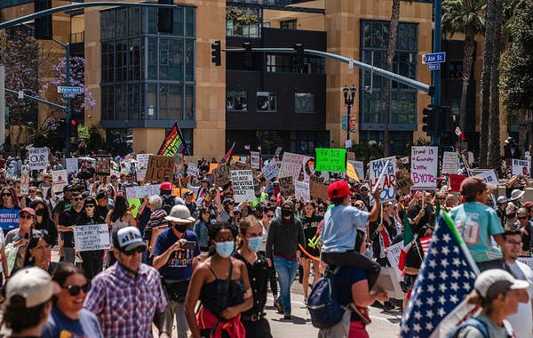A diverse crowd of protesters holding signs marches in a city street, advocating for various causes