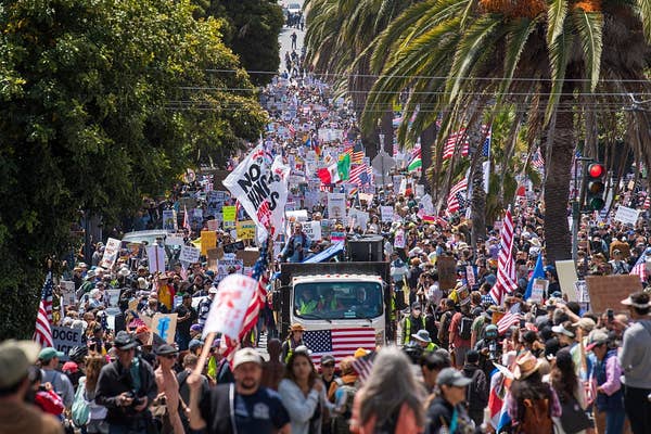 A large crowd of people march in protest on a city street, holding signs and flags