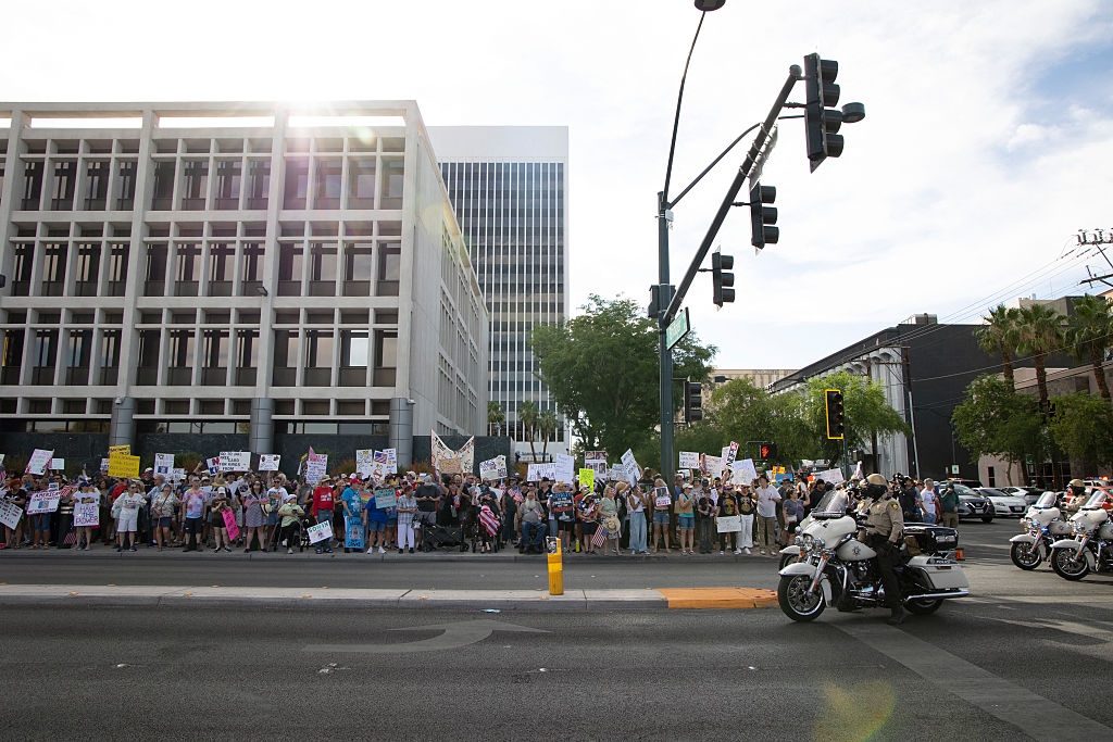 Large crowd of protesters with signs on a city street, observed by police officers on motorcycles
