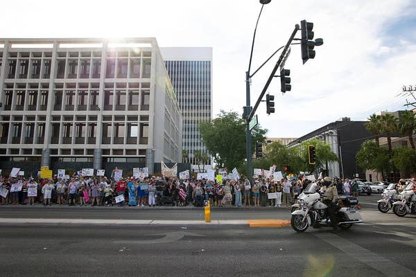 Large crowd of protesters with signs on a city street, observed by police officers on motorcycles