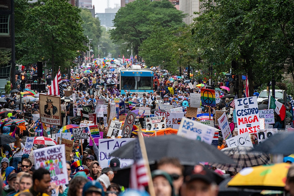 Large crowd of protesters holding various signs and banners on a city street, advocating for diverse social and political causes