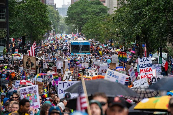 Large crowd of protesters holding various signs and banners on a city street, advocating for diverse social and political causes