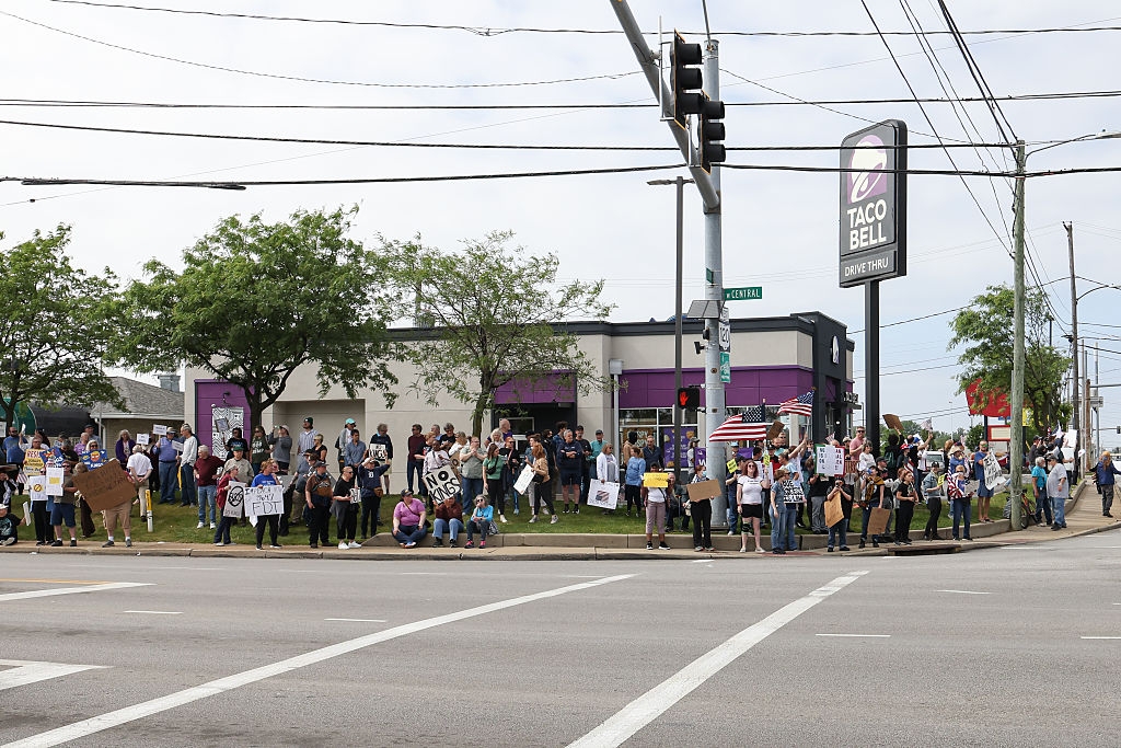 Crowd of protesters with signs gathered outside a Taco Bell at a street corner