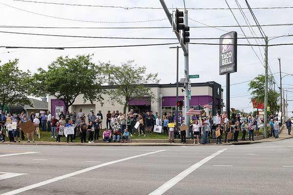 Crowd of protesters with signs gathered outside a Taco Bell at a street corner