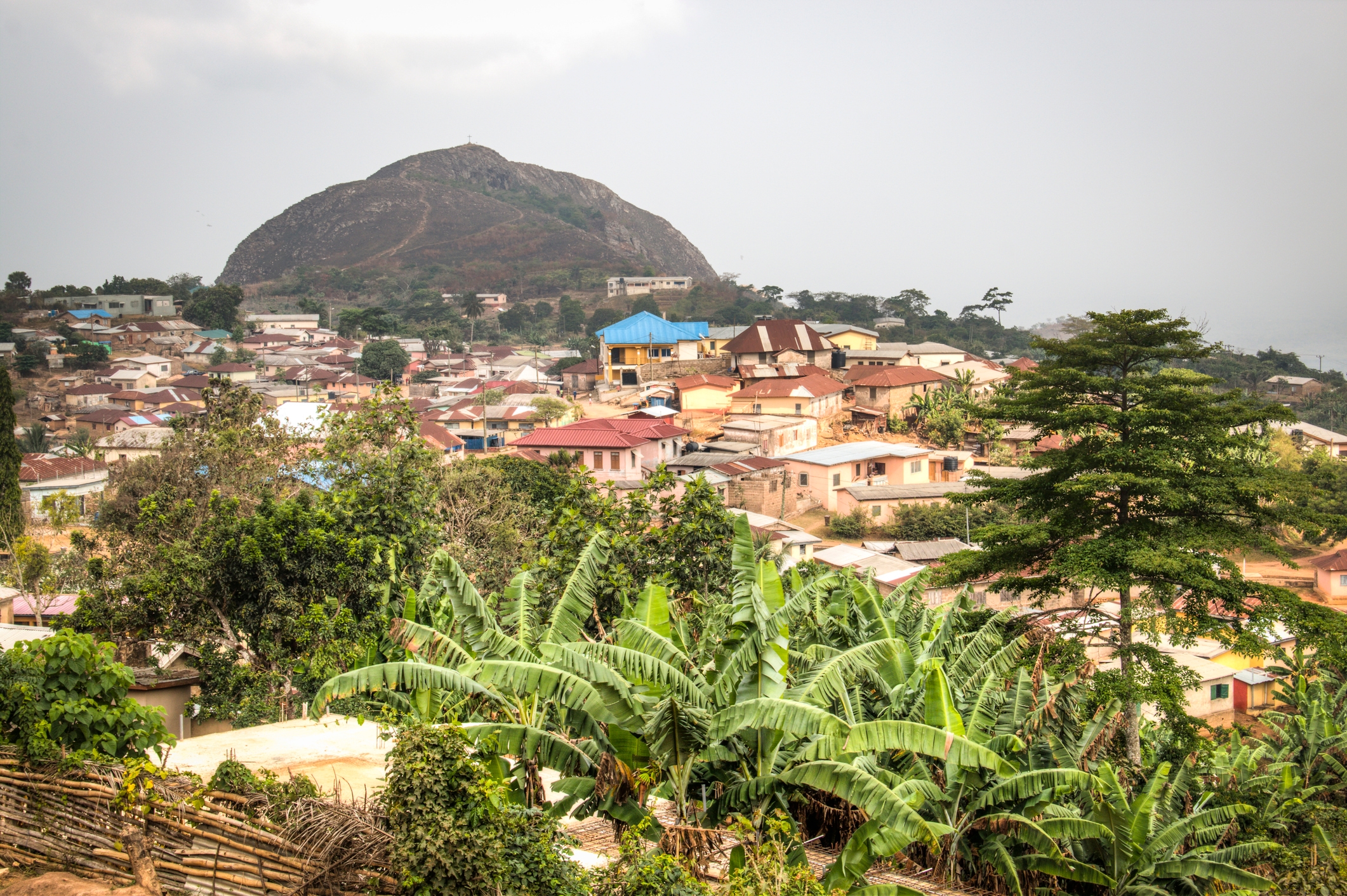 Scenic view of a hillside village with lush greenery and scattered houses, with a large hill in the background