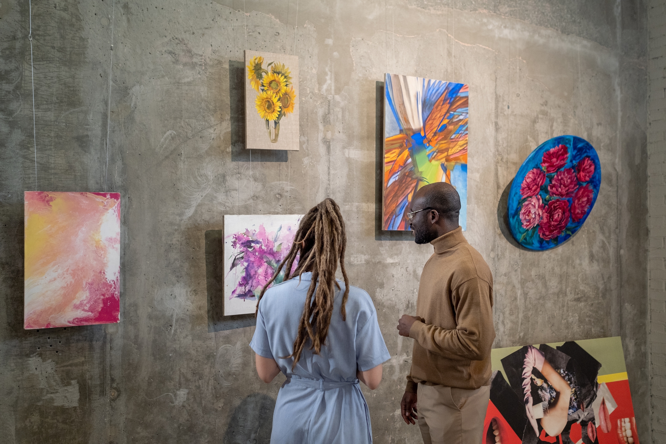 Two people view colorful abstract art on a gallery wall with concrete texture