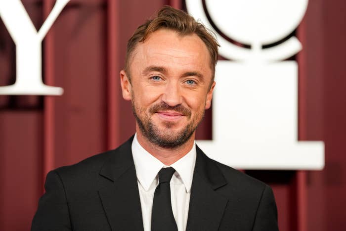 Man in suit and tie at a formal event, smiling in front of a backdrop with large letters