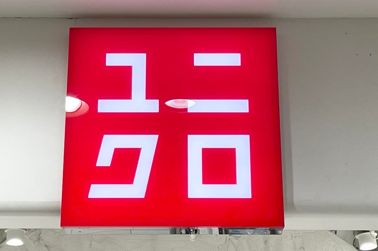 Sign with stylized characters and logo, possibly of a Japanese clothing brand, on a red background in a store interior