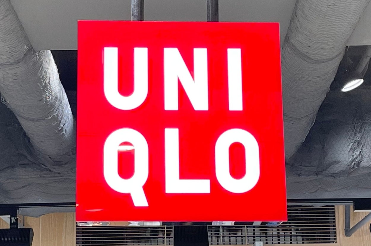 Uniqlo store interior with a red hanging sign. Shelves below display folded clothes priced at 3,990 yen