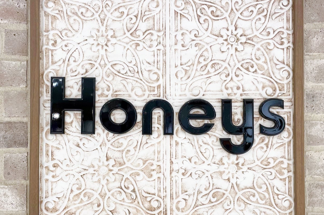 レンガの壁に「Honeys」と書かれた装飾的な看板が取り付けられている。