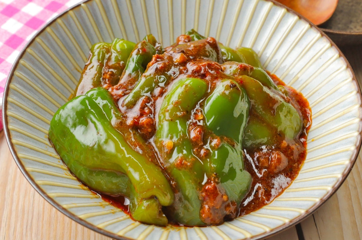 お皿に盛られたピーマンと肉の炒め物。白と青のストライプの陶器に盛られ、背景に木製テーブルとチェック柄の布がある。