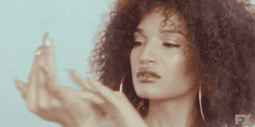 Person with curly hair and hoop earrings examines their nails with an expressive look