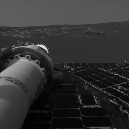 Rover captures Martian landscape with part of its equipment and solar panel visible in the foreground. Rocky terrain extends to the horizon