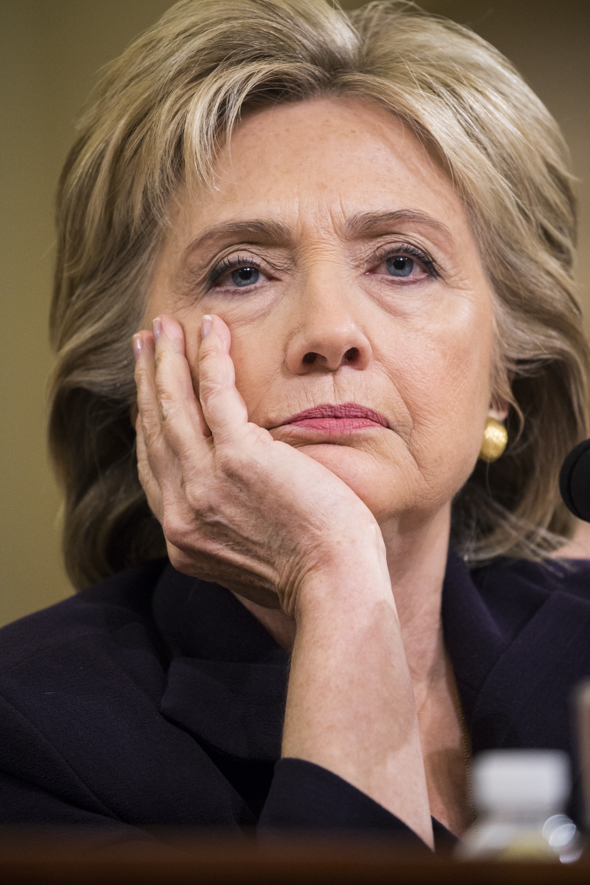 Person with a thoughtful expression, resting chin on hand, in formal attire during a public hearing