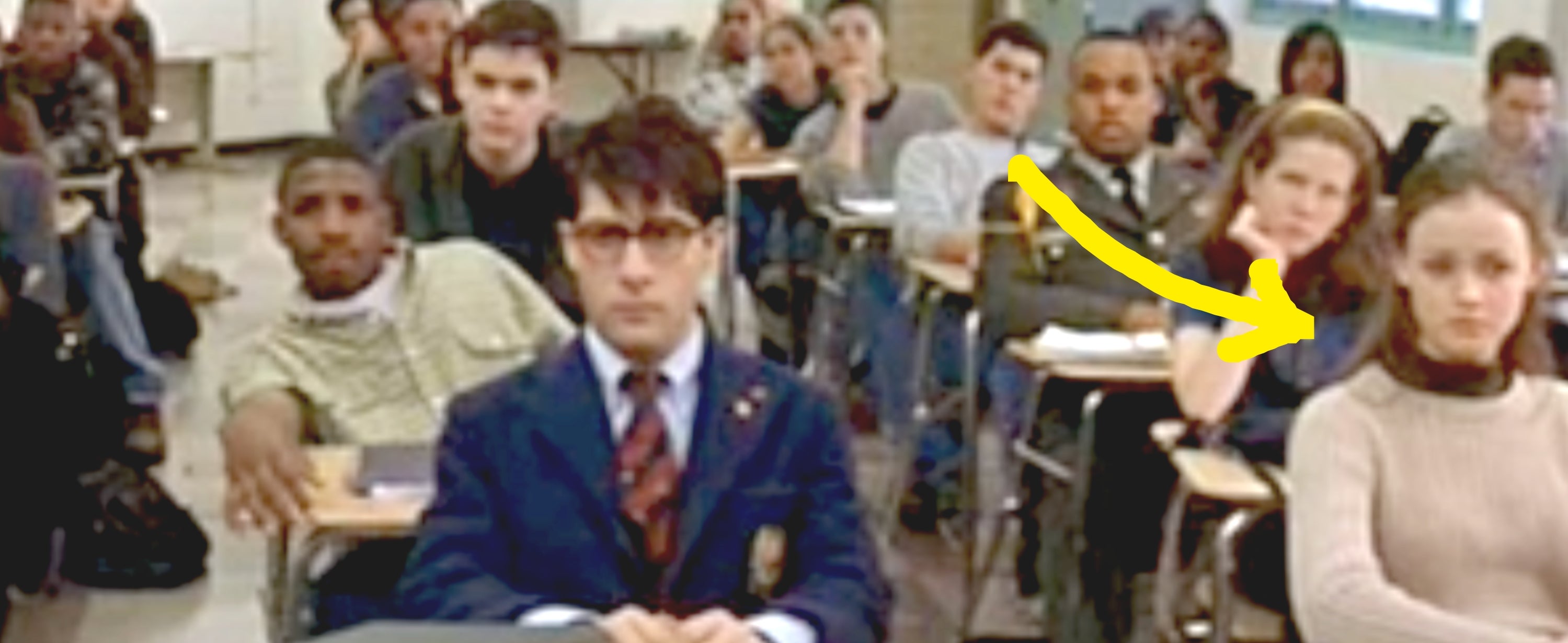 Classroom scene with students seated at desks, attentively facing forward; one student wears a blazer and tie
