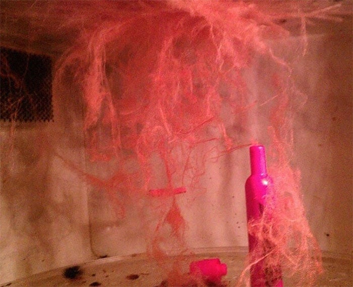 Melted lipstick in a microwave with pink wax streaks hanging from the top, creating a chaotic, abstract pattern