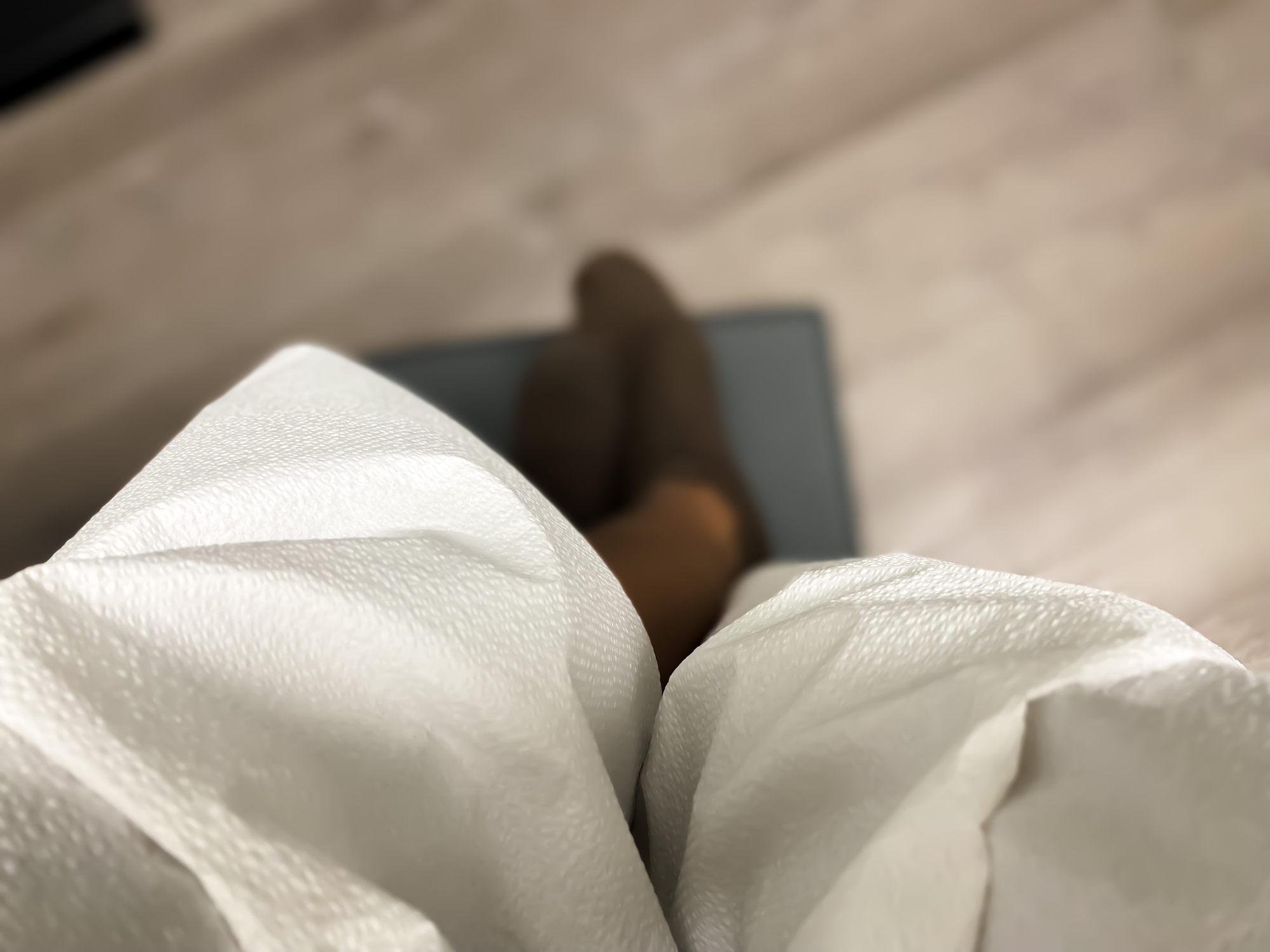 Uklart utsikt over en person som har på seg lysfargede bukser og brune sko, sitter med ben krysset på en stol