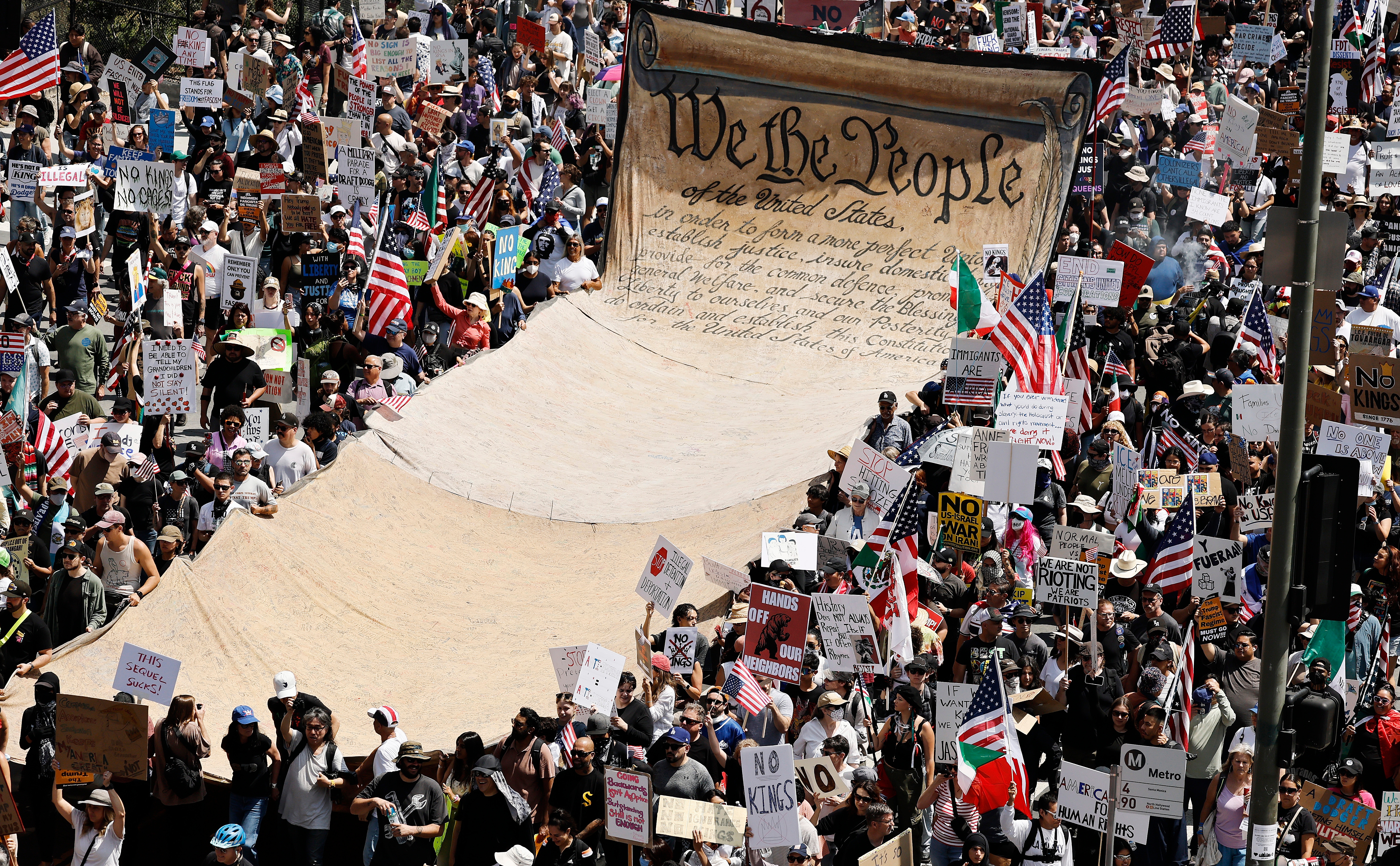 Large protest crowd holding signs and flags. A giant replica of the U.S. Constitution&#x27;s &quot;We the People&quot; is prominently displayed
