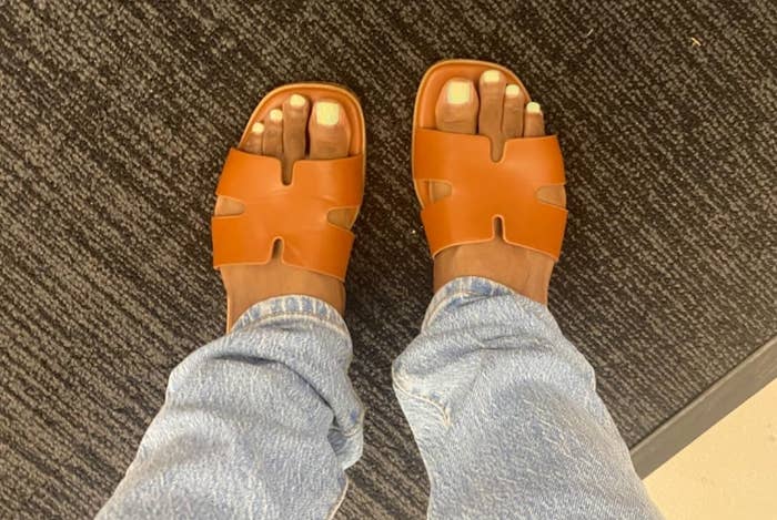 Person wearing brownish sandals and airy bluish jeans, lasting connected a textured floor.