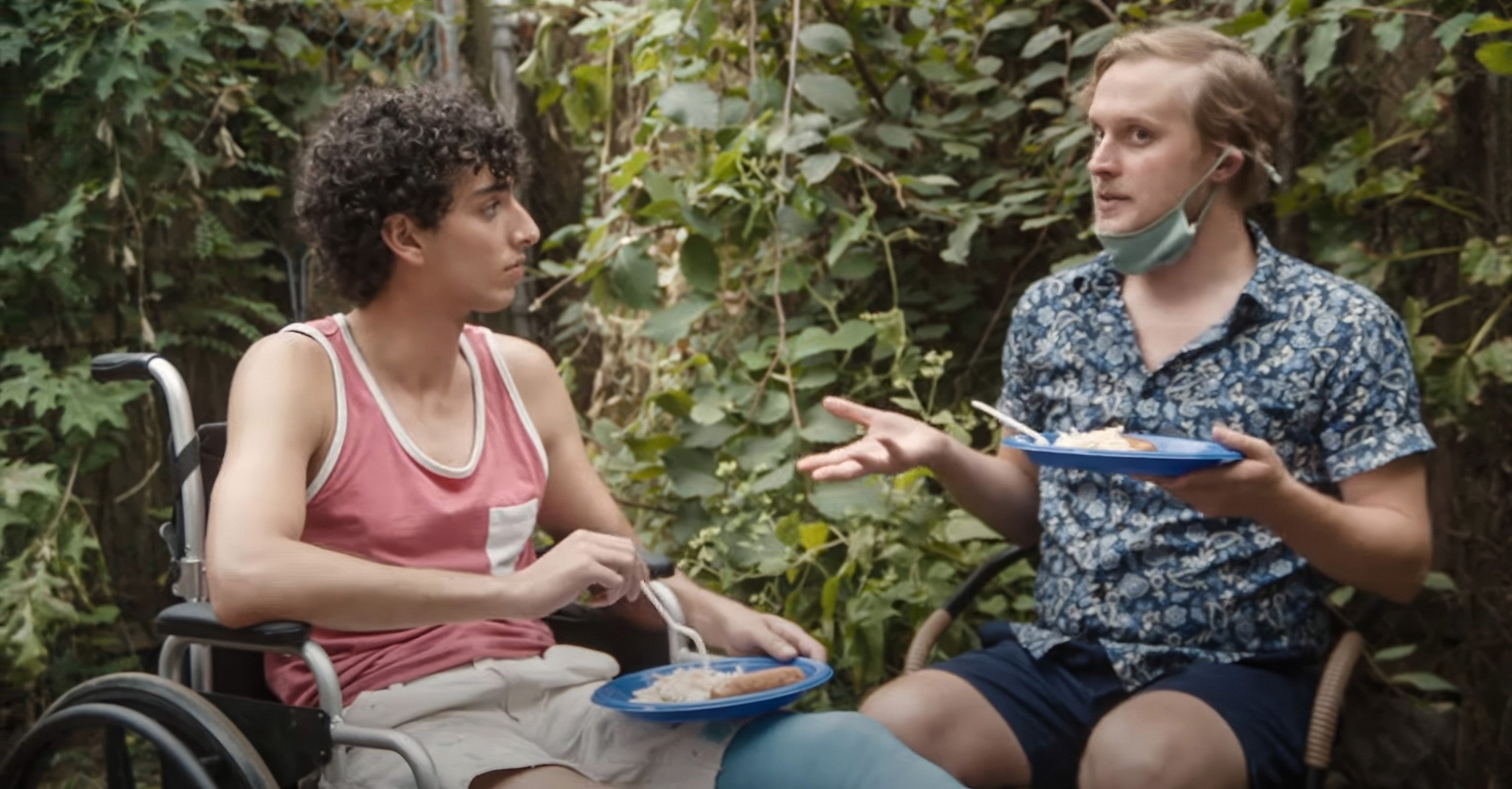 Two individuals outdoors, 1  successful  a wheelchair wearing a vessel  top, the different   seated adjacent    successful  shorts, holding a disguise  and gesturing portion    talking