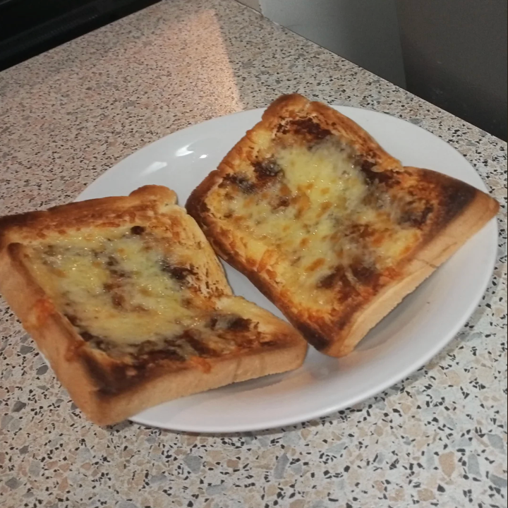 Two slices of toast with dissolved cheese on a white plate, placed on a discotop