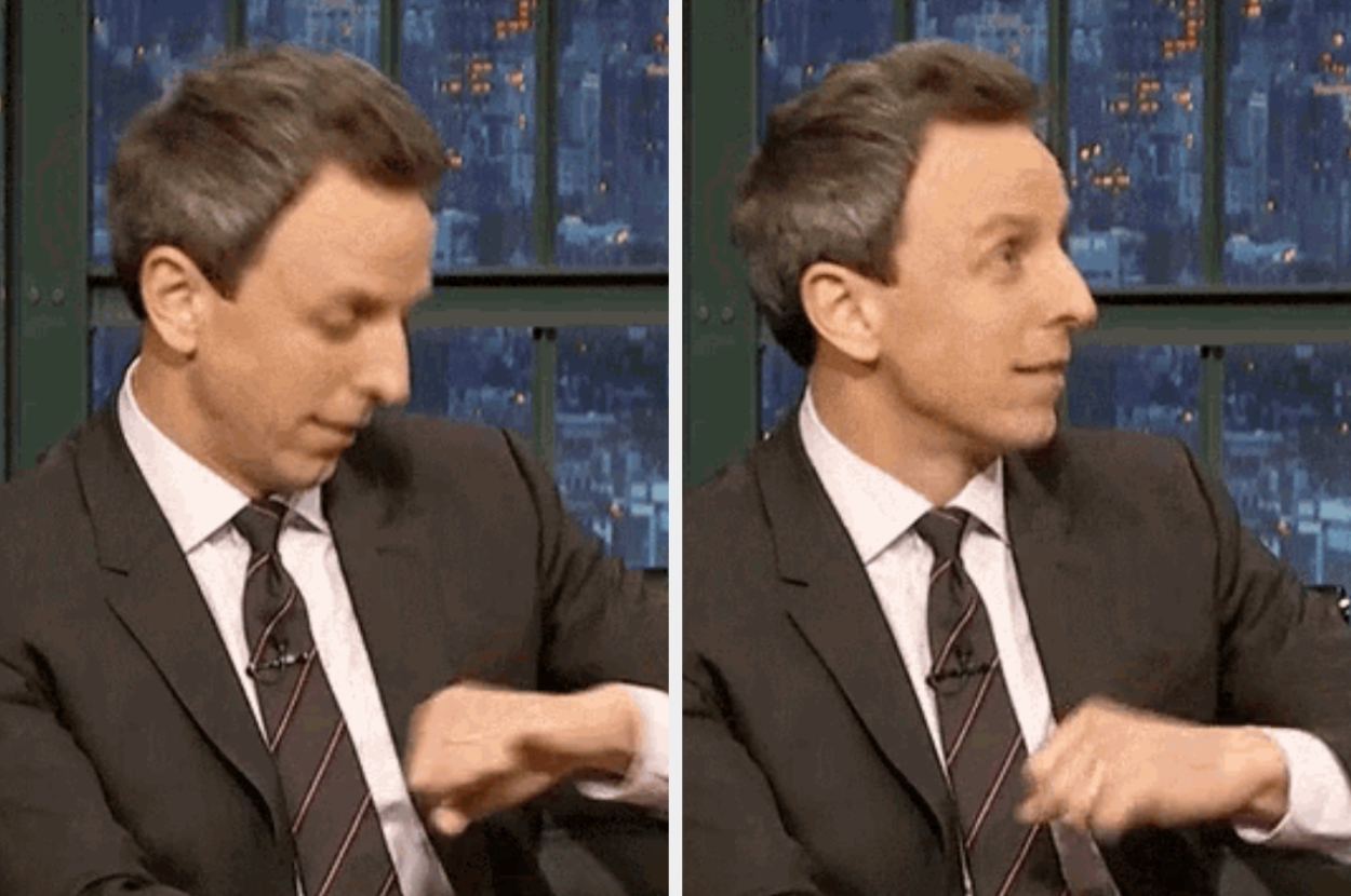 Seth Meyers in a suit looking down at a watch, then straight ahead, on a talk show set