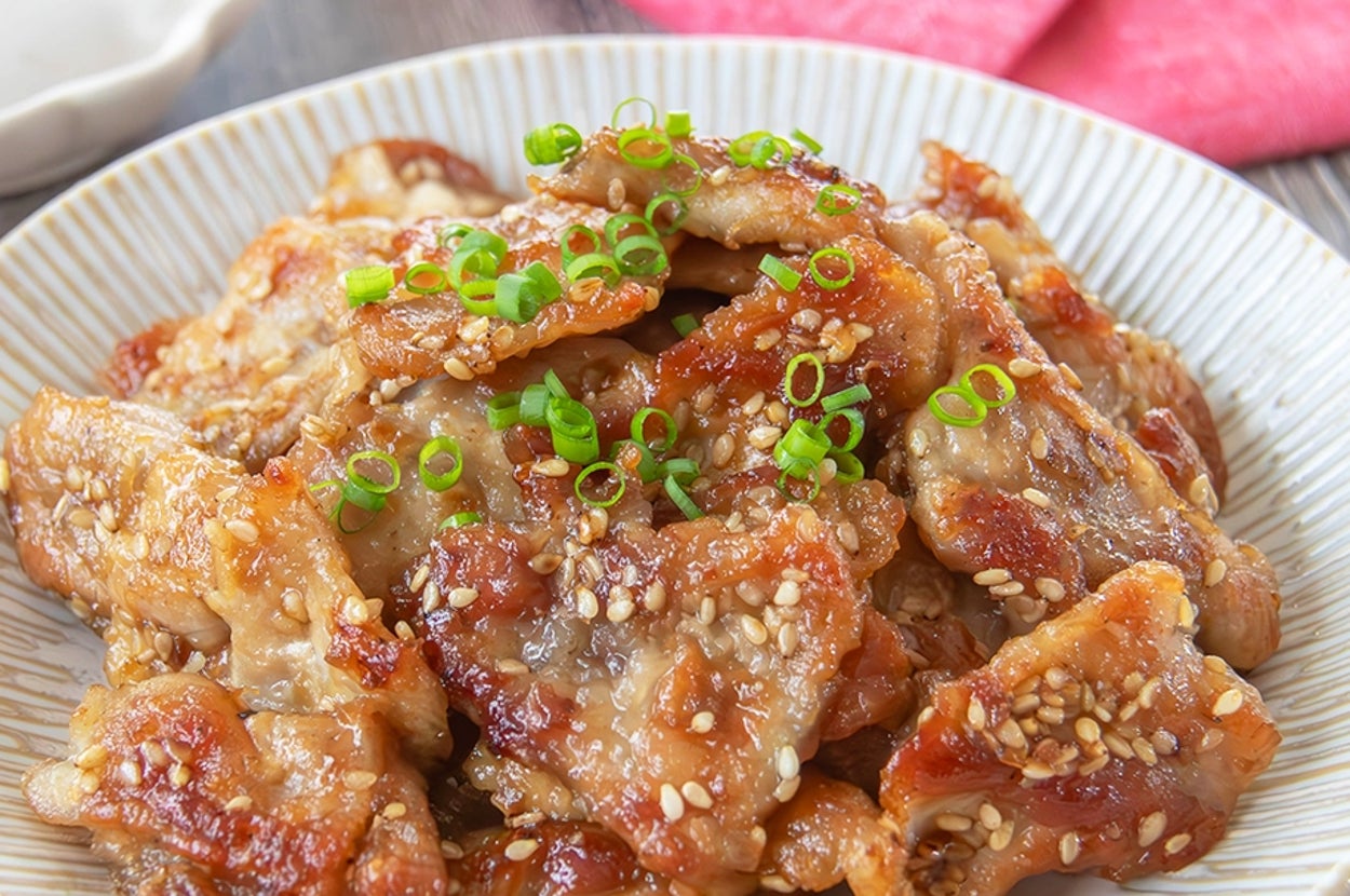 お皿に盛られたごまと和風のたれが絡んだカリカリの豚こま肉。小ネギがトッピングされている。