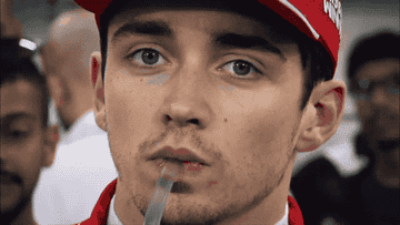 Person in a red cap and jacket with a thoughtful expression, holding a straw in their mouth. Background shows blurred people