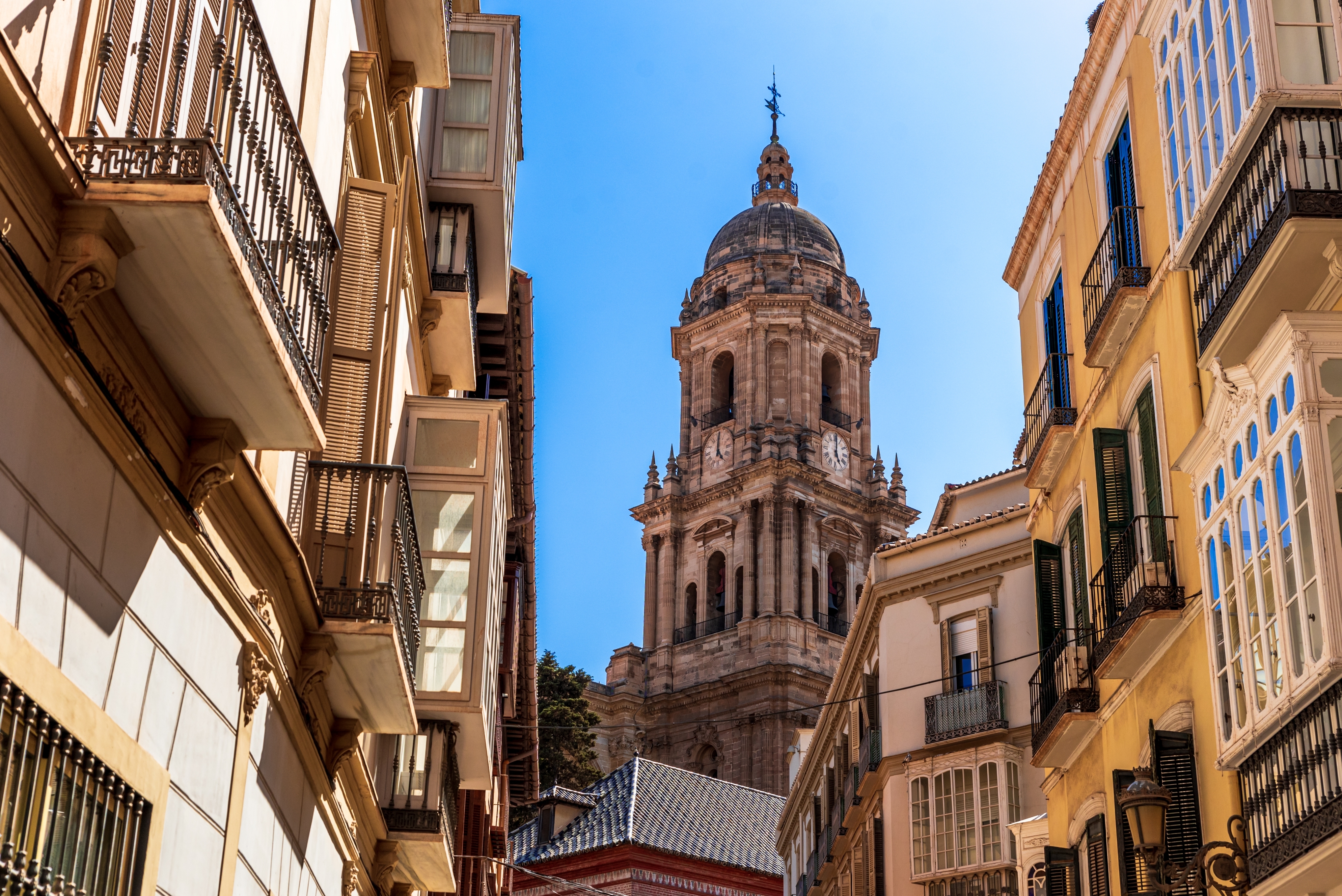 Street view of a historic European city with a prominent cathedral tower surrounded by traditional architecture