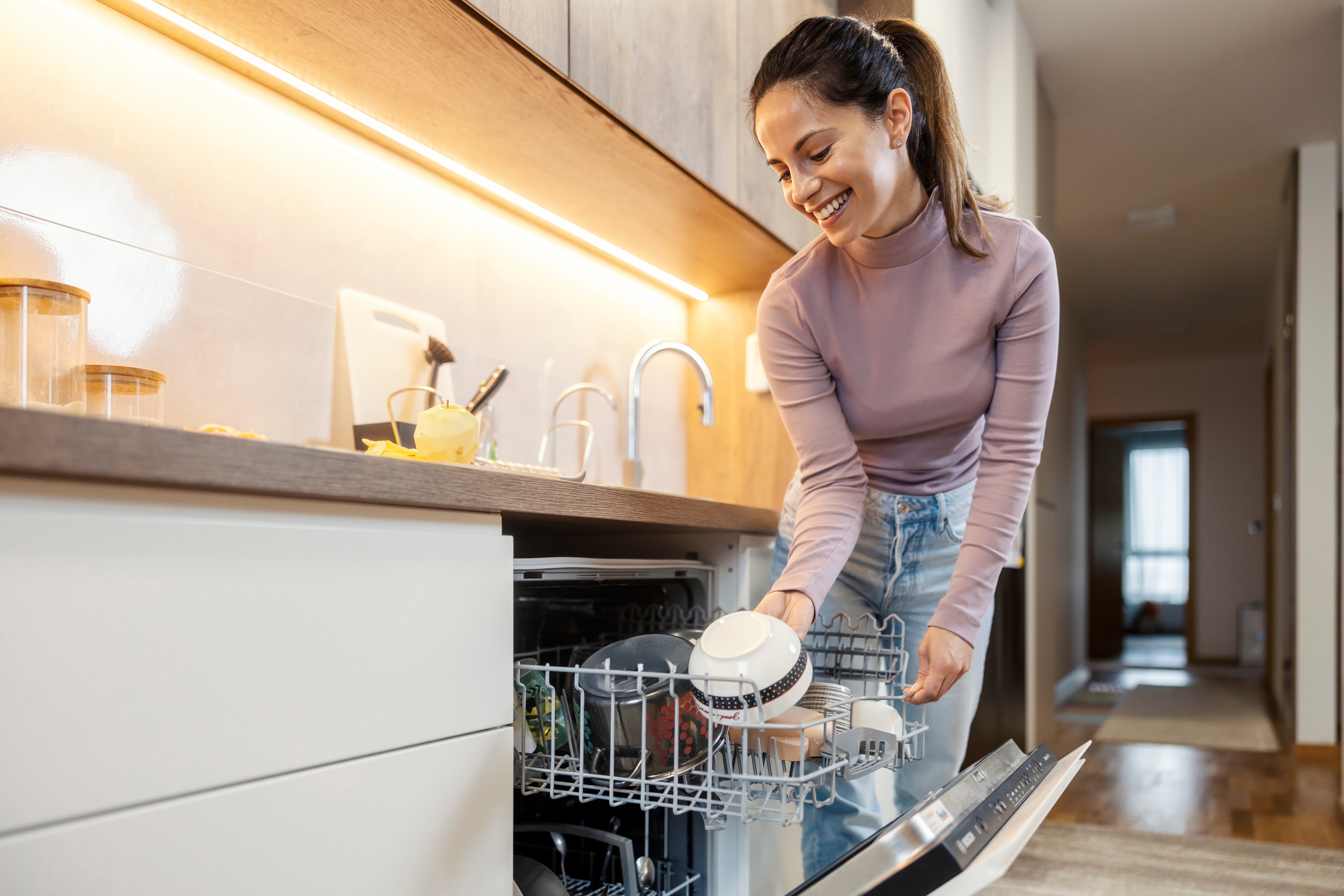 Person Lossing en oppvaskmaskin, plasserer rene retter på disken på et moderne kjøkken
