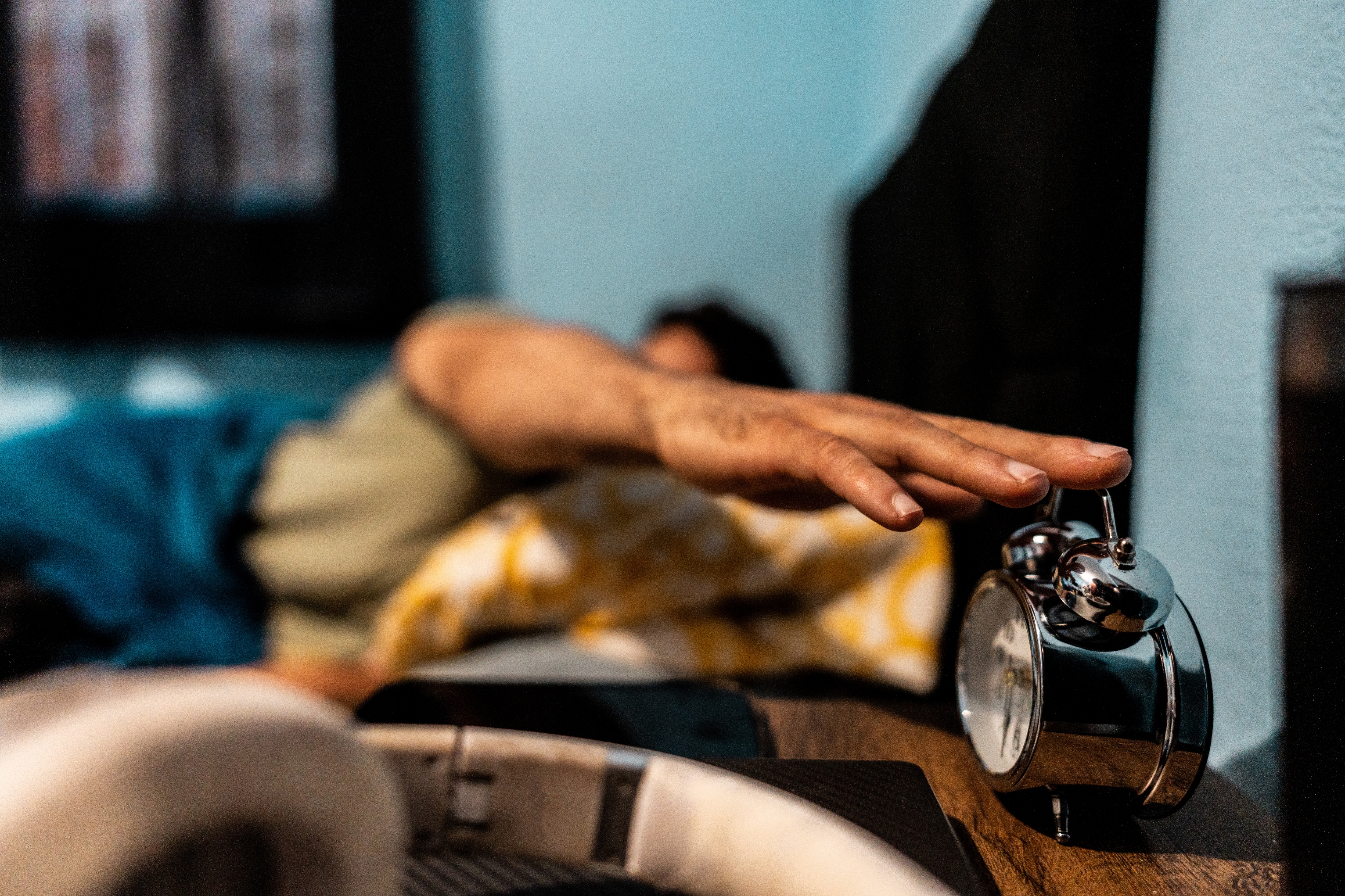 Personen som strekker seg for å slå av en vekkerklokke i sengen. Scenen foreslår å våkne opp tidlig på morgenen